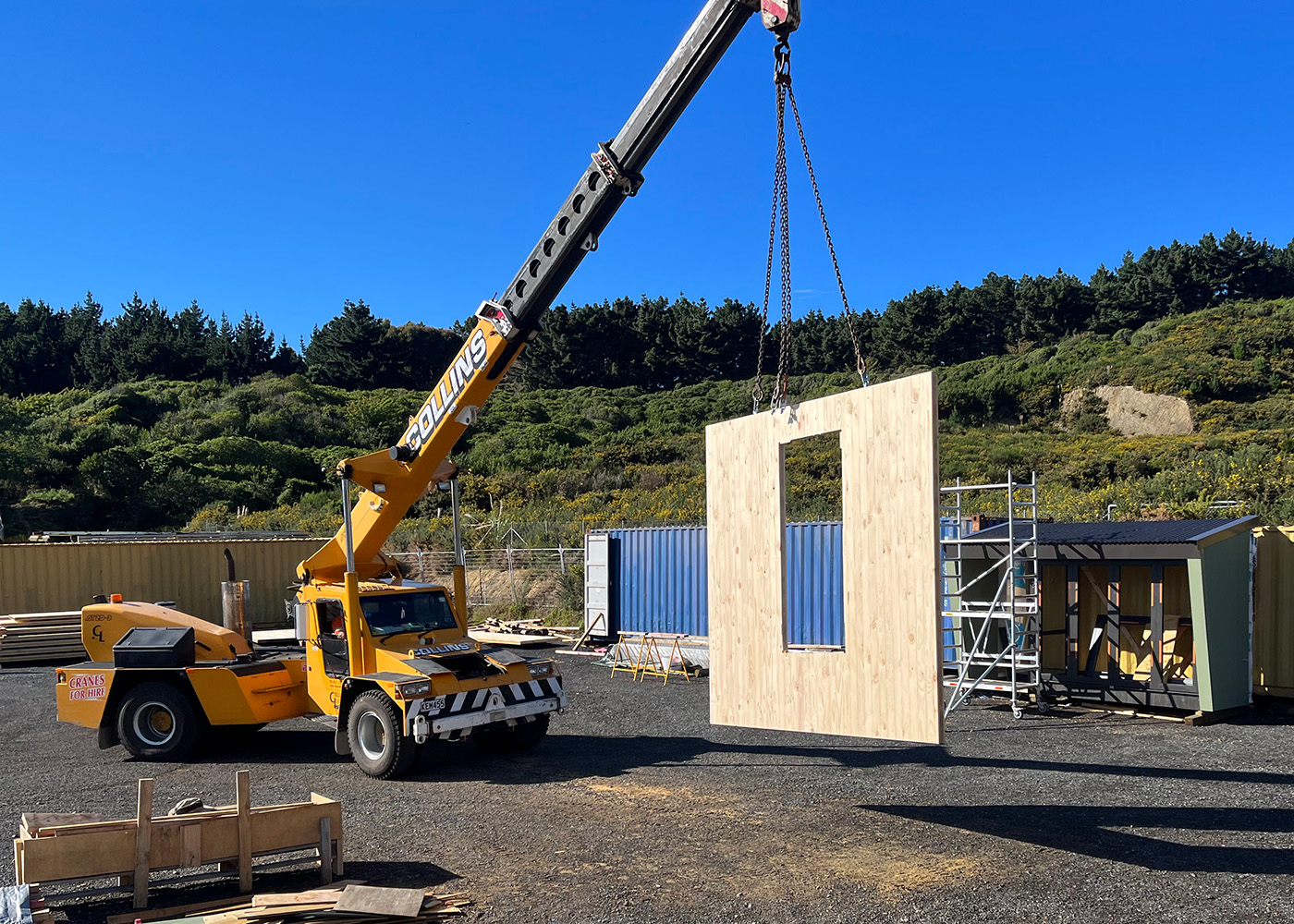Crane lifting panel into place for Te Whare-iti module at assembly site in Porirua.