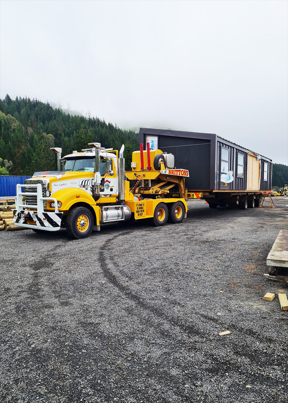 Truck with completed building on board leaves assembly site to transport to customer's site.